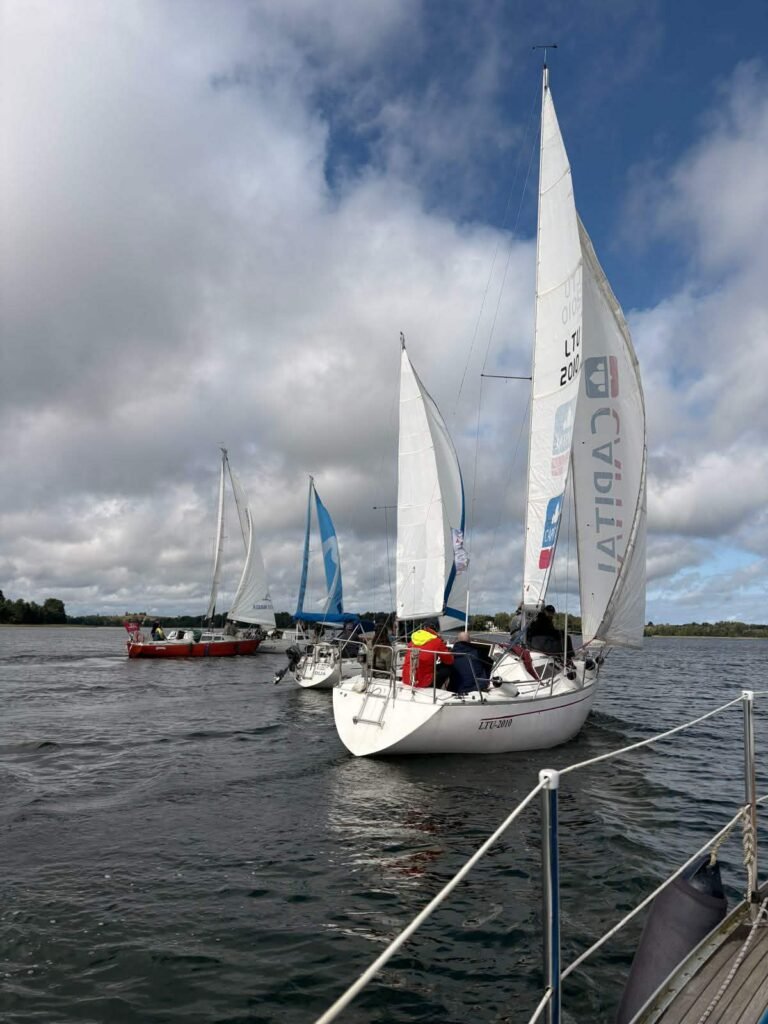 Jachtų regata Trakuose – jachtos plaukia viena paskui kitą, vaizdas iš jachtos denio